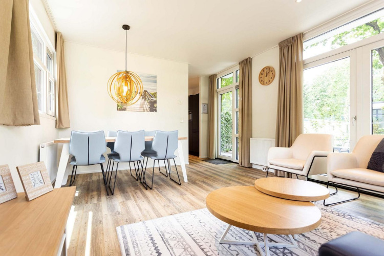 Alojamiento glamping luminoso con diseño moderno, mesa de comedor, sillones cómodos y grandes ventanales.