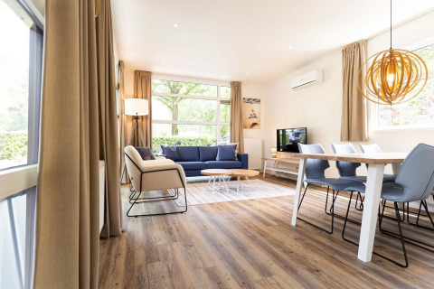 Moderne glamping accommodatie met lichte inrichting, houten vloer, eettafel, zetel en grote ramen.