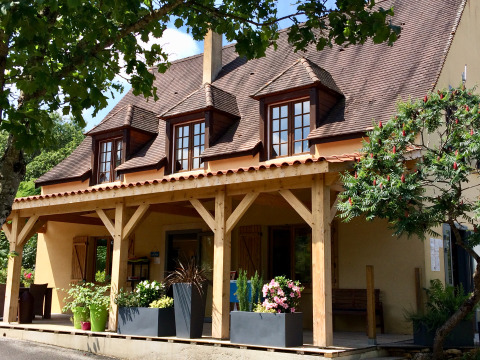 Vista frontal de Camping Les Charmes - Cottages Dordogne con porche, vigas de madera y macetas con flores.