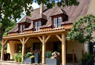 Front view of Camping Les Charmes - Cottages Dordogne featuring a porch, wooden beams, and potted plants.