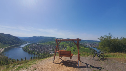 Ausblick vom Hügel bei Kröv, Deutschland, mit einer Schaukelbank, Fahrrad und der Mosel im Panorama.
