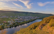 Udsigt over floden og byen Kröv, omgivet af bakker og vinmarker i Rheinland-Pfalz, Tyskland ved solnedgang.