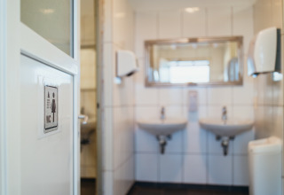 Entrada a un baño femenino con dos lavabos, espejo y dispensadores en Paradies Camp, Renania-Palatinado.