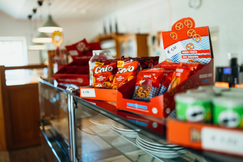 Kleurrijke snack- en pretzelverpakkingen op een glazen toonbank in Paradies Camp, vakantiepark in Rijnland-Palts.