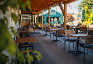 Overdekt buitenterras met houten tafels en stoelen bij Paradies Camp, Rijnland-Palts, Duitsland.