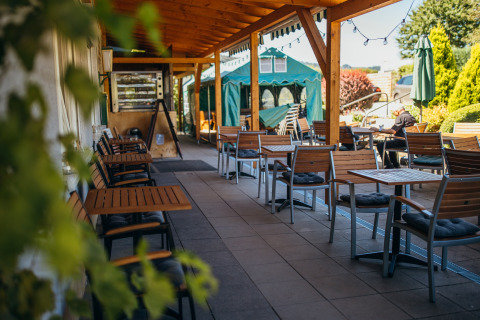 Terrasse couverte avec tables et chaises au Paradies Camp en Rhénanie-Palatinat, Allemagne, par temps ensoleillé.