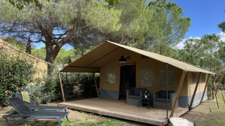 Tienda safari en Camping le Mas de Mourgues, Francia, con terraza de madera y zona de descanso exterior.