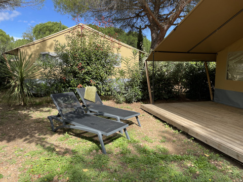 Dos tumbonas junto a una tienda safari en Camping le Mas de Mourgues, Francia, rodeadas de vegetación.