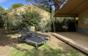 Two loungers by a safari tent at Camping le Mas de Mourgues in France, surrounded by greenery and trees.