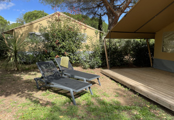 Two loungers by a safari tent at Camping le Mas de Mourgues in France, surrounded by greenery and trees.