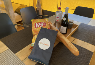 Mesa en una tienda safari en Camping le Mas de Mourgues, Francia, con vino, pan, agua y patatas fritas.