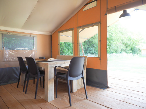 Binnenkant van een safaritent met houten tafel, zwarte stoelen en grote ramen met zicht op de natuur.