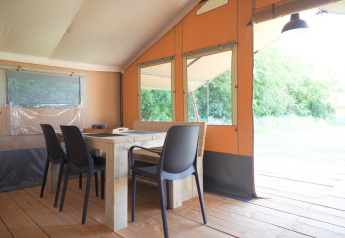 Interior of a safari tent featuring a wooden table, black chairs, and large windows with a nature view.