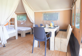 Vista interior de una tienda safari con suelo de madera, mesa de comedor y dormitorio con literas.