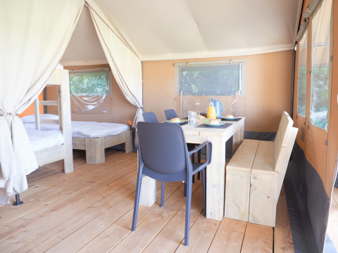 Vista interior de una tienda safari con suelo de madera, mesa de comedor y dormitorio con literas.