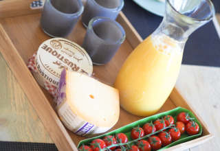Ontbijtmand met sap, tomaatjes, kaas, camembert en drie blauwe bekers in een safaritent.