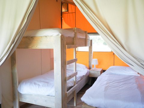 Vista interior de una tienda safari con litera, cama doble, sábanas blancas y cortinas abiertas a los lados.