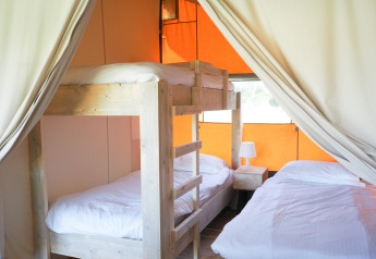 Interior of a Safari tent showing a bunk bed, double bed, white linens, and curtains drawn to the sides.