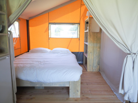 Interior de tienda safari con cama doble, muebles de madera y paredes naranjas, ideal para glamping acogedor.