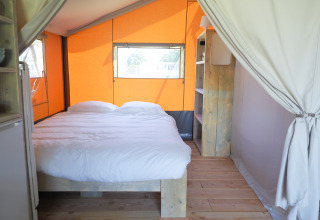 Binnenkant van een safaritent met een tweepersoonsbed, houten meubels en oranje canvas, ideaal voor glamping.