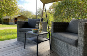 Cozy outdoor sitting area with wicker chairs and table, in front of a safari tent at Camping Paradis La Bretonniere, France.