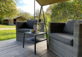 Zona de estar exterior con sillas de mimbre frente a tienda safari en Camping Paradis La Bretonniere, Francia.