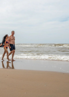 Pareja camina descalza por la playa junto al mar en parque vacacional con opciones de glamping.