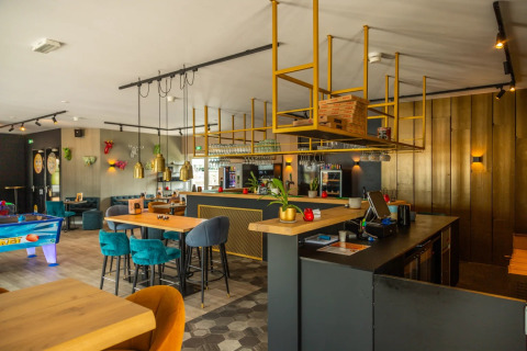 Moderna zona de bar y salón en un parque vacacional con interiores elegantes, sillas coloridas y juegos.