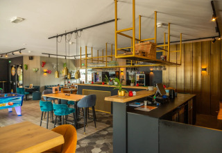 Moderna zona de bar y salón en un parque vacacional con interiores elegantes, sillas coloridas y juegos.