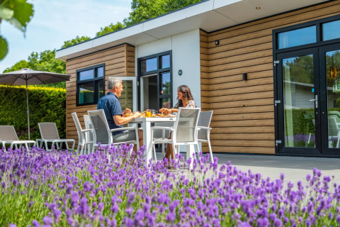 Couple partageant un repas devant une cabane glamping moderne au parc de vacances avec lavande en premier plan.