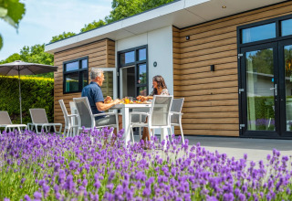 Couple partageant un repas devant une cabane glamping moderne au parc de vacances avec lavande en premier plan.