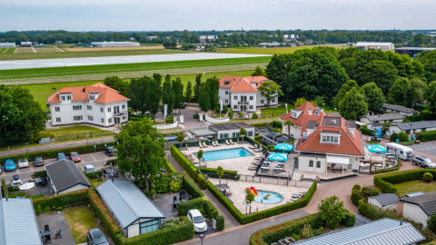 Feriepark med glamping, swimmingpool, villaer og grønne områder, tæt på en landingsbane i naturskønne omgivelser.
