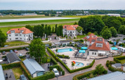 Feriepark med glamping, swimmingpool, villaer og grønne områder, tæt på en landingsbane i naturskønne omgivelser.
