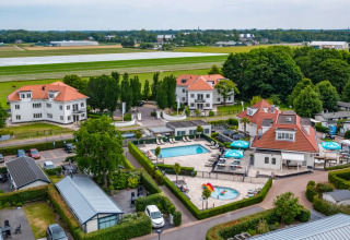 Feriepark med glamping, swimmingpool, villaer og grønne områder, tæt på en landingsbane i naturskønne omgivelser.
