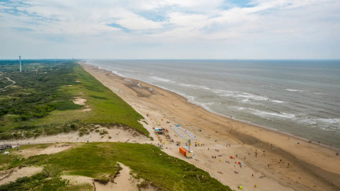 Vue large sur une plage de sable, des dunes et la mer, prise depuis un parc de vacances proposant du glamping.