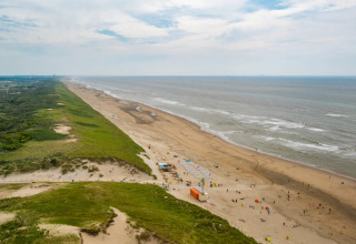 Groot uitzicht op strand, duinen en zee, genomen bij een vakantiepark met glamping accommodaties aan de kust.