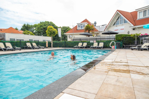 Piscina exterior con dos personas, tumbonas y alojamientos de glamping en un parque vacacional.