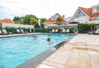 Piscine extérieure avec deux personnes, transats et hébergements glamping dans un parc de vacances.