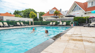 Piscina exterior con dos personas, tumbonas y alojamientos de glamping en un parque vacacional.