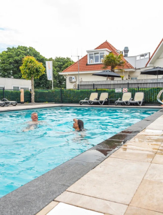 Piscina exterior con dos personas, tumbonas y alojamientos de glamping en un parque vacacional.