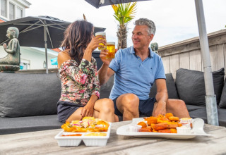 Twee mensen proosten en genieten van snacks op het terras van een vakantiepark met glamping.