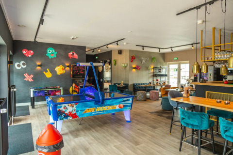 Binnenlounge op een vakantiepark met arcadespellen, moderne zitplaatsen en kleurrijke wanddecoraties.