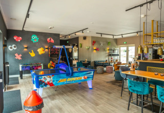 Binnenruimte in een vakantiepark met arcadespellen, moderne zitjes en opvallende, kleurrijke decoratie.