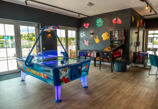 Spillerum på en feriepark med glamping, med airhockey, bordfodbold og flippermaskine indendørs.