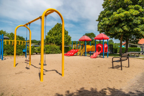 Parco giochi con altalene e scivoli in un villaggio turistico che offre glamping, in una giornata di sole