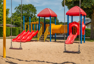 Kleurrijke speeltuin met glijbanen en schommels, gelegen in een vakantiepark met glamping faciliteiten.