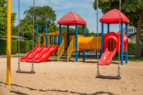 Kleurrijke speeltuin met glijbanen en schommels, gelegen in een vakantiepark met glamping faciliteiten.