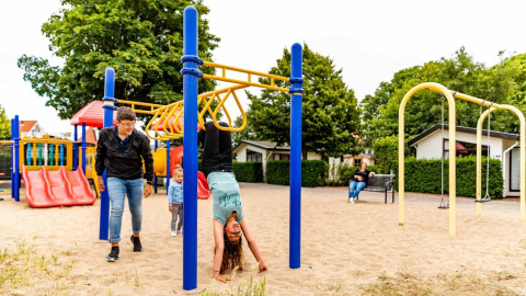 Niños juegan en un parque infantil de un parque vacacional con alojamientos glamping, rodeados de árboles.