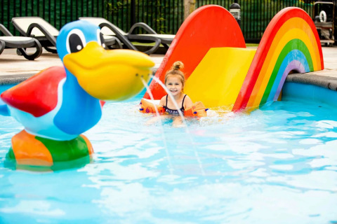 Klein meisje speelt in zwembad met regenboogglijbaan en grote eend bij een vakantiepark met glamping.