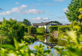 A cozy glamping cabin by a calm canal, surrounded by lush greenery at a holiday park on a sunny day.